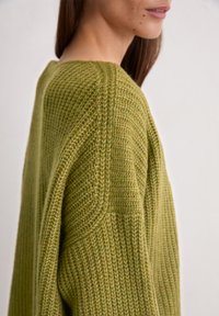 Olijfgroen gebreid sweater met een losse pasvorm, voorzien van een textuurpatroon en verlaagde schouders, wat de zachte en comfortabele uitstraling benadrukt.