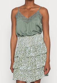 Grüne Satin-Camisole mit Spitzensaum, kombiniert mit einem tiered Rüschensrock, der ein leicht grünes und weißes abstraktes Muster aufweist.