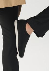 Svart strikket slip-on sko med hvit gummisåle. Designet har en tettsittende passform rundt ankelen og et teksturert overmateriale.