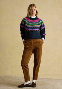 Pletený sveter s mnohobarevným vzorom, obsahujúci námornícku modrú, ružovú, zelenú a žltú farbu. Skombinovaný s hnedými kordurovými nohavicami a tmavými mokasínami.