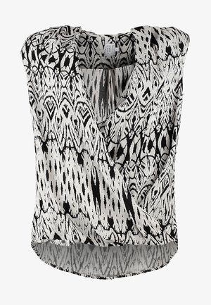 Haut sans manches noir et blanc avec un design enveloppant, présentant des motifs géométriques ; associé à un pantalon noir et des bottines.