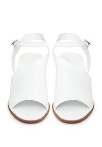 Weiße Ledersandalen mit kreuzgefügtem Vorderdesign, offener Zehenpartie und verstellbarem Knöchelriemen. Braune Sohle, glatte Textur, minimalistischer Stil.