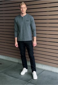 Grå långärmad henley-skjorta med krage, ihop med mörka jeans och vita sneakers. Bakgrunden har bruna träplankor.