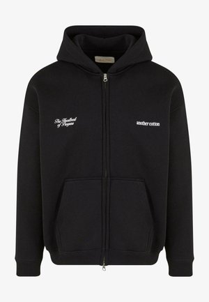 Musta tõmblukkudega kapuutsiga särk, mis on valmistatud puuvillast. Omab eesmist taskut, ribaga mansette ja kahte valgete tikanditega fraasi rinnal.