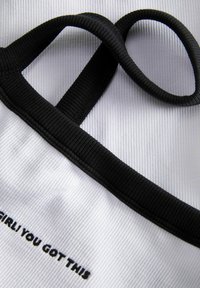 Witte stof met een ribbeltextuur heeft een zwarte elastische band en de tekst "GIRLI YOU GOT THIS" in zwarte stiksel.