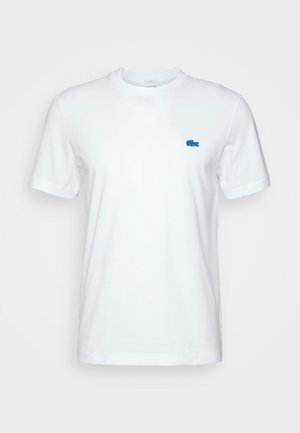 Biała koszulka z krótkim rękawem i okrągłym dekoltem, z małym niebieskim logo krokodyla na lewej piersi.