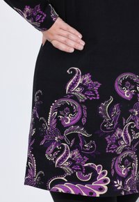 Tunique noire avec des motifs floraux paisley en violet et crème, dotée d'un ourlet arrondi et d'un tissu doux et texturé.