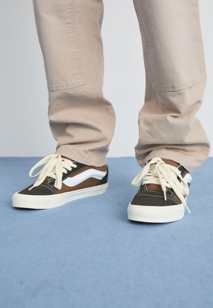 Brown and black canvas sneakers with white accents, featuring a low-top design, round laces, and textured rubber soles.