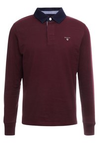 Burgundské polo tričko s dlouhým rukávem, tmavě modrým límcem, jedním bílým knoflíkem a malým bílým logem GANT na levé hrudi.