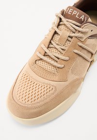 Sneakers beiges en mesh et daim. Comprennent des coutures détaillées, un design perforé sur le bout, et des lacets texturés.