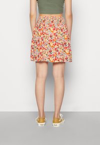 Saia floral com flores vermelhas, laranjas e amarelas sobre um fundo claro; cintura elástica; combinada com sapatos bege.