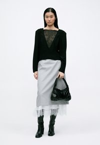 Maglietta nera a maniche lunghe con scollatura in pizzo trasparente, abbinata a una gonna grigia chiara e stivali neri fino al ginocchio. Tiene una borsa nera con texture.