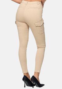 Pantalones cargo beige con un diseño ajustado, que cuentan con bolsillos laterales y traseros, combinados con zapatos de tacón alto negros y puntiagudos.