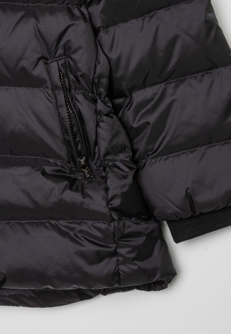 Czarna kurtka puchowa z przeszytymi panelami, zamkiem błyskawicznym w kieszeni i ściągaczami na mankietach, wykonana z lśniącego, lekkiego materiału syntetycznego.