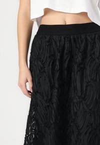 Jupe noire avec un motif texturé en vagues. Dotée d'une large ceinture noire, elle est fabriquée à partir d'un tissu léger et fluide.