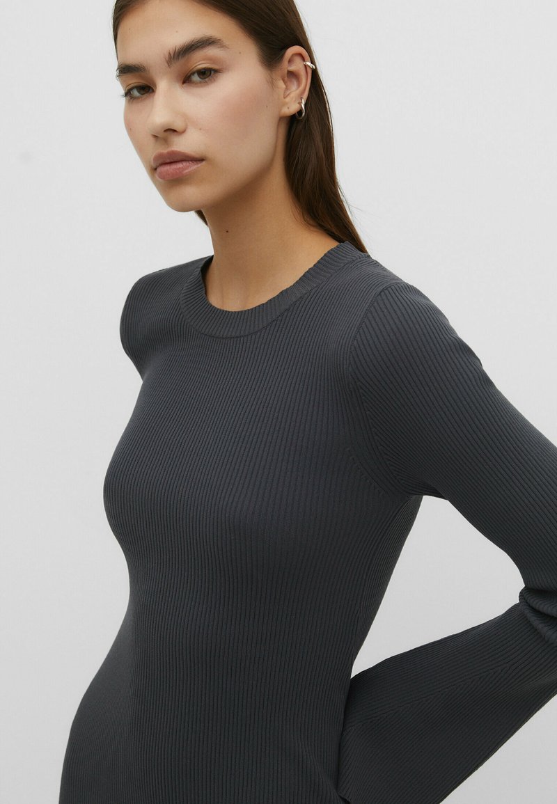 Rippenshirt mit langen Ärmeln in Dunkelgrau. Verfügt über einen runden Ausschnitt und eine taillierte Silhouette. Der Stoff hat eine glatte Textur mit dezentem Stretch.