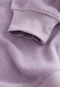 Close-up af en lyse lilla fleeceærme med ribbet manchet, der viser blødt, tekstureret stof og detaljerede syninger.