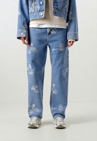 Svijetloplave traperice s bijelim grafičkim uzorcima. Opusten kroj, pet džepova, i ravne nogavice. Uparene s srebrnim tenisicama.