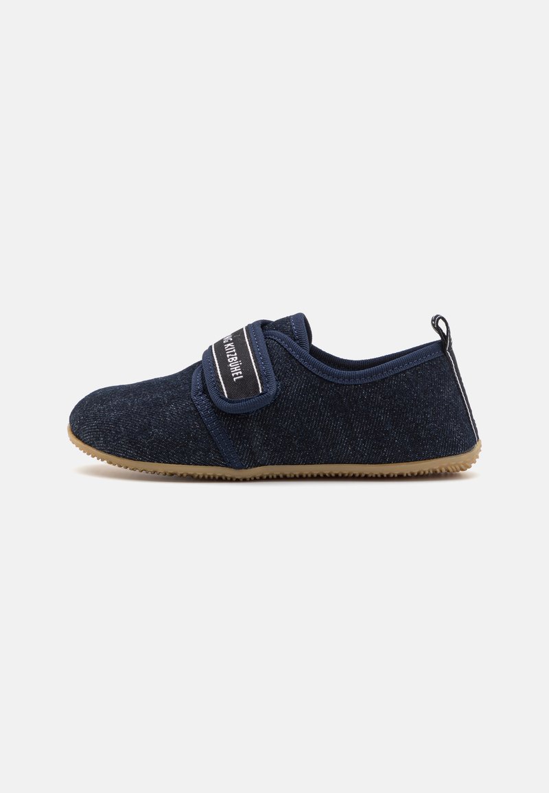 Sapato slip-on de tecido azul-marinho com uma superfície texturizada, faixa elástica na parte superior e sola de borracha com fundo em tom bege.