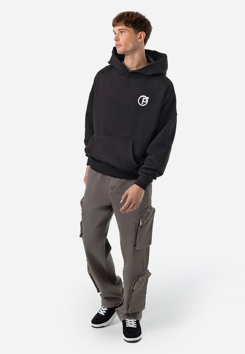 Black hoodie with front pocket and logo, paired with light gray cargo pants featuring zippered pockets, and black sneakers with white soles.