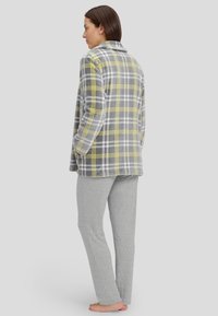 Chaqueta de forro polar de cuadros grises con acentos amarillos, combinada con pantalones grises claros que tienen un patrón de puntos. Ambos artículos son de corte holgado.