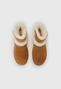Bottines en suède marron avec une douce doublure en shearling blanc et un revers. Le design présente une pointe arrondie et une semelle plate.