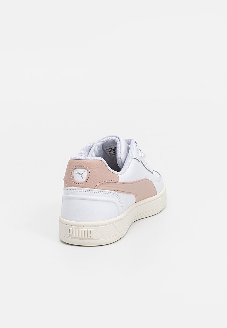Baskets blanches avec des accents roses, fabriquées en matériau synthétique. Équipées d'une semelle en caoutchouc texturée et d'un logo sur le talon et sur le côté.