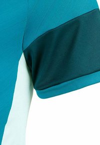 Camisa deportiva en color verde azulado con un patrón texturizado. Acento de manga en un verde azulado oscuro con un acabado suave. Diseño de corte ajustado y panel lateral en contraste.