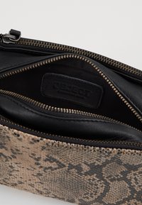 Interno di una borsa elegante con cerniera, caratterizzata da una fodera in pelle nera e un esterno in stampa serpente beige texturizzato.