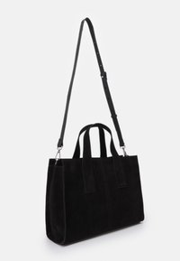 Czarna zamszowa torba typu tote z dwiema krótkimi rączkami i regulowanym, odczepianym długim paskiem na ramię na białym tle.