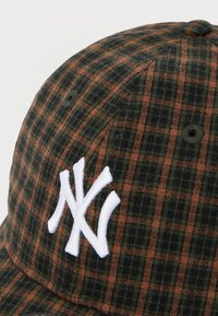 Σκούφος σε σκούρο πράσινο και καφέ καρό με λευκό κεντημένο λογότυπο των New York Yankees. Διαθέτει υφασμάτινη υφή και λεπτομέρεια με κουμπί στην κορυφή.