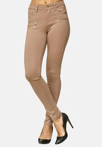 Tunna beige byxor i mjukt tyg, med två fickor med dragkedja och en slät yta. Matcher med svarta högklackade skor.