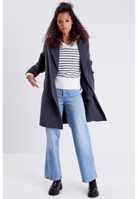 Abrigo de mezcla de lana en color carbón con botones de doble botonadura, superpuesto sobre un suéter rayado blanco y marino, combinado con jeans acampanados en azul claro y botas negras.