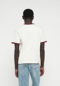 Λευκή μπλούζα με μπορντό γιακά και μανσέτες, κοντά μανίκια και στρογγυλή λαιμόκοψη. Συνδυασμένη με ανοιχτό μπλε τζιν παντελόνι.