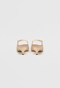 Paire de chaussures slingback beige à talons bas avec fines lanières, vue de dos sur un fond clair uni.