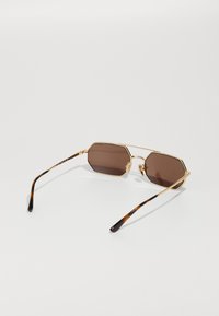 Ochelari de soare octogonali cu lentile maro și ramă din metal auriu. Brațele au un model din scoică de țestoasă. Design ușor și elegant.