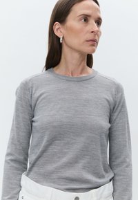 Pull gris à manches longues en matière douce, doté d'un col rond et d'une texture subtile, associé à un pantalon blanc à taille haute.