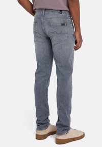 Slim-fit grijze denim jeans met een vijf-pocket ontwerp, voorzien van subtiele stikselaccenten, en gecombineerd met lichtbeige sneakers.