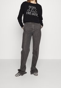 Felpa nera con testo bianco "REBEL & Rule BREAKER", abbinata a jeans grigi a gamba dritta e scarpe con punta a forma di zebrastrisce.