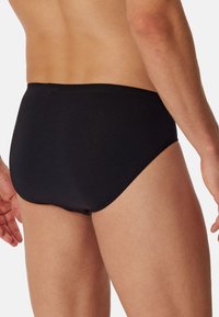 Calzoni da nuoto neri realizzati in tessuto liscio e elastico, con una vestibilità aderente e un design semplice senza modelli o decorazioni visibili.