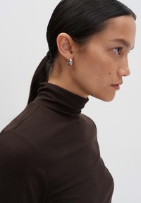 Zilveren ringoorbellen met een gepolijste afwerking, gedragen aan het oor van een model. De donkere bruine coltrui van het model heeft een geribbelde textuur.