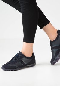 Granatowe buty sportowe z zamszu i materiałów syntetycznych. Wyposażone w szare paski, teksturowaną podeszwę oraz niski profil.