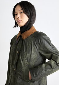 Γυαλιστερό πράσινο υφασμάτινο μπουφάν με καφέ κοτλέ γιακά, κλείσιμο με κουμπιά και τσέπες. Διαθέτει δομημένο σχέδιο και διακριτική γυαλάδα.