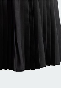 Falda negra plisada con un tejido texturizado, que presenta pliegues uniformes y bordes limpios. El material parece liviano y finamente tejido.