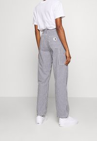 Spodnie w paski mają pionowe paski w kolorze granatowym i białym, wysoki stan, dwie boczne kieszenie oraz małą naszywkę z logo na tylnej kieszeni.