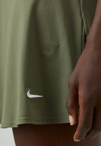 Falda Nike verde olivo con una textura suave, que presenta un logo blanco cerca del dobladillo y una abertura lateral para ofrecer mayor libertad de movimiento.