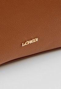 Surface en cuir brun texturé avec de petites lettres en métal doré épelant "LCREDI" fixées près du bas au centre.