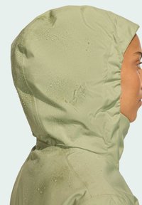 Svetlozelená nepremokavá bunda s priliehavou kapucňou, na povrchu sú vidieť kvapky vody a má hladkú matnú textúru.