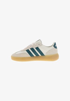 Baskets basses beige avec des bandes Adidas vert foncé et une semelle en caoutchouc gomme, vues de profil sur un fond blanc.