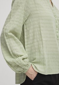 Hellgrüne Bluse aus strukturierter Stoff, mit V-Ausschnitt, Knöpfen und voluminösen Ärmeln mit elastischen Bündchen.